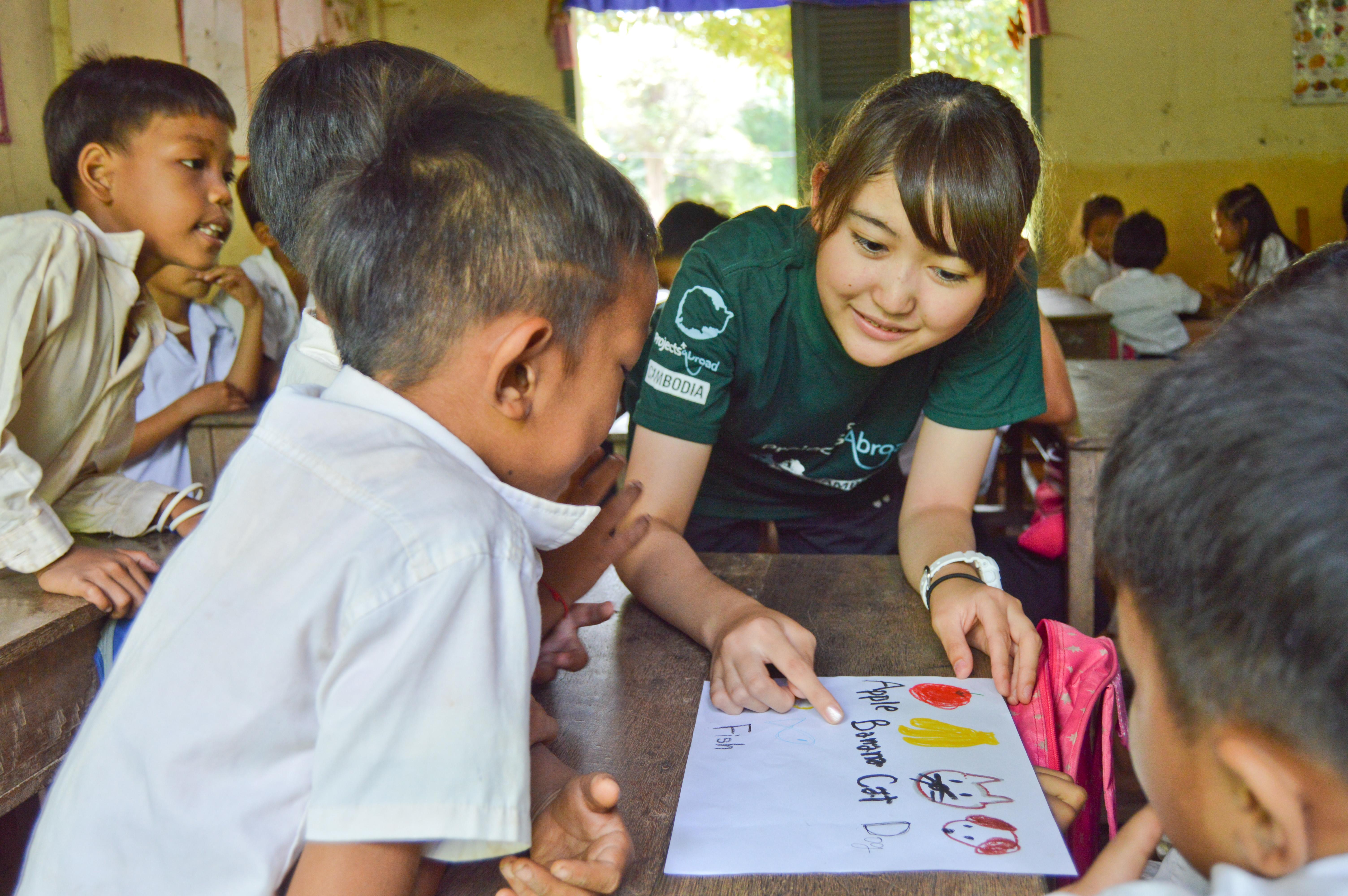 A Projects Abroad teenage community volunteer working in Cambodia helps a child with his English pronunciation. A teenage volunteer working with children in Cambodia helps a child with his English animal and fruit sight words.